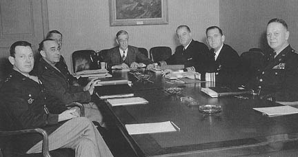 Réunion du JRDB le mercredi 11 février 1948. On distingue de gauche à droite : le major-général L. C.    Craigie, le général Joseph T. McNarney, le général Jacob L. Devers, le docteur Vannevar Bush (président du JRBD), le vice-amiral E. W. Mills, le vice-admiral J. D. Price    et le lieutenant-général H. S. Arnold